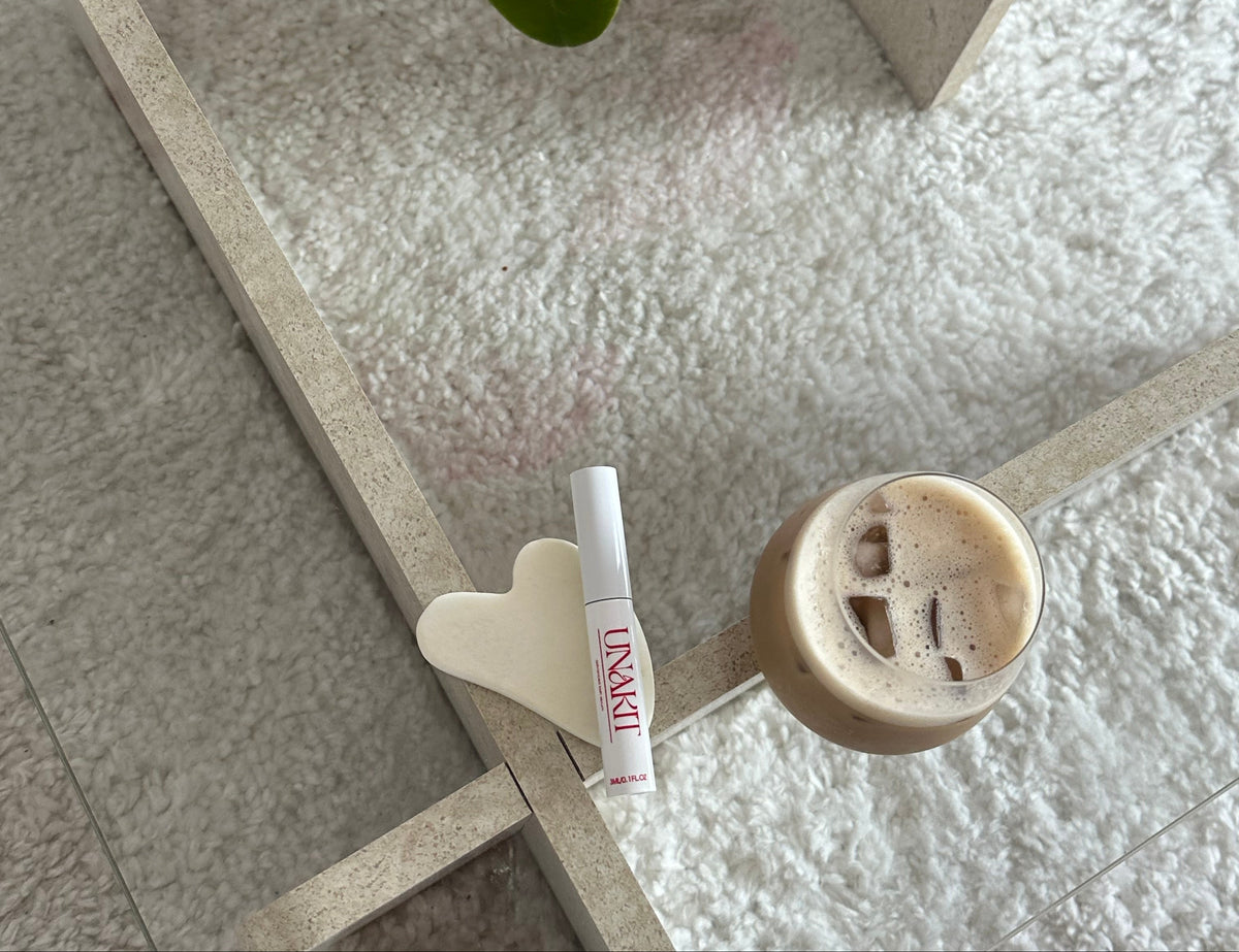 UNAKIT lash serum beside a cup of coffee
